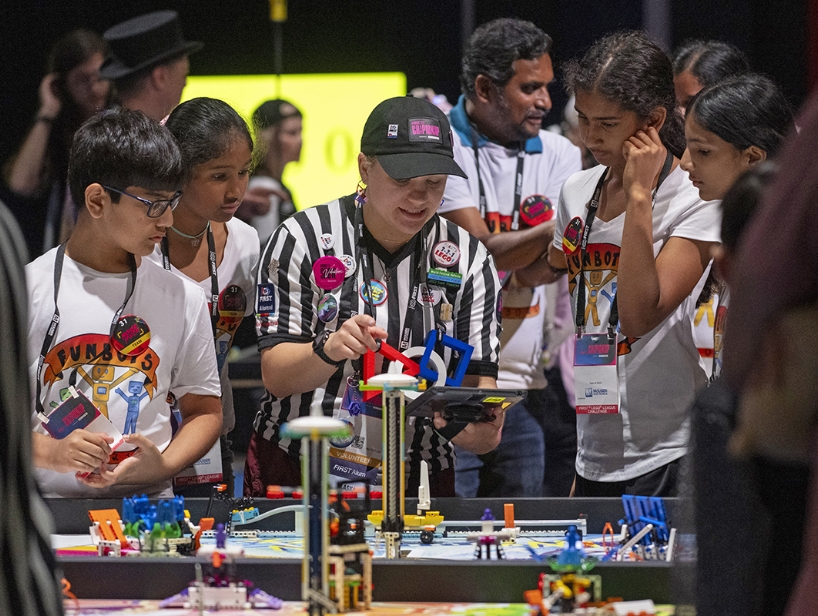A coach helps children participate in a FIRST event.
